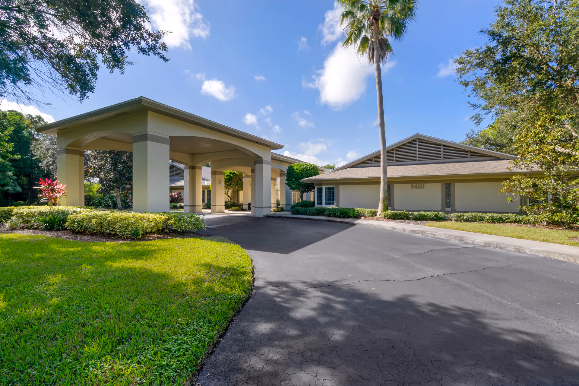 Exterior view of a senior living facility entrance with a covered porte-cochere and landscaping.
