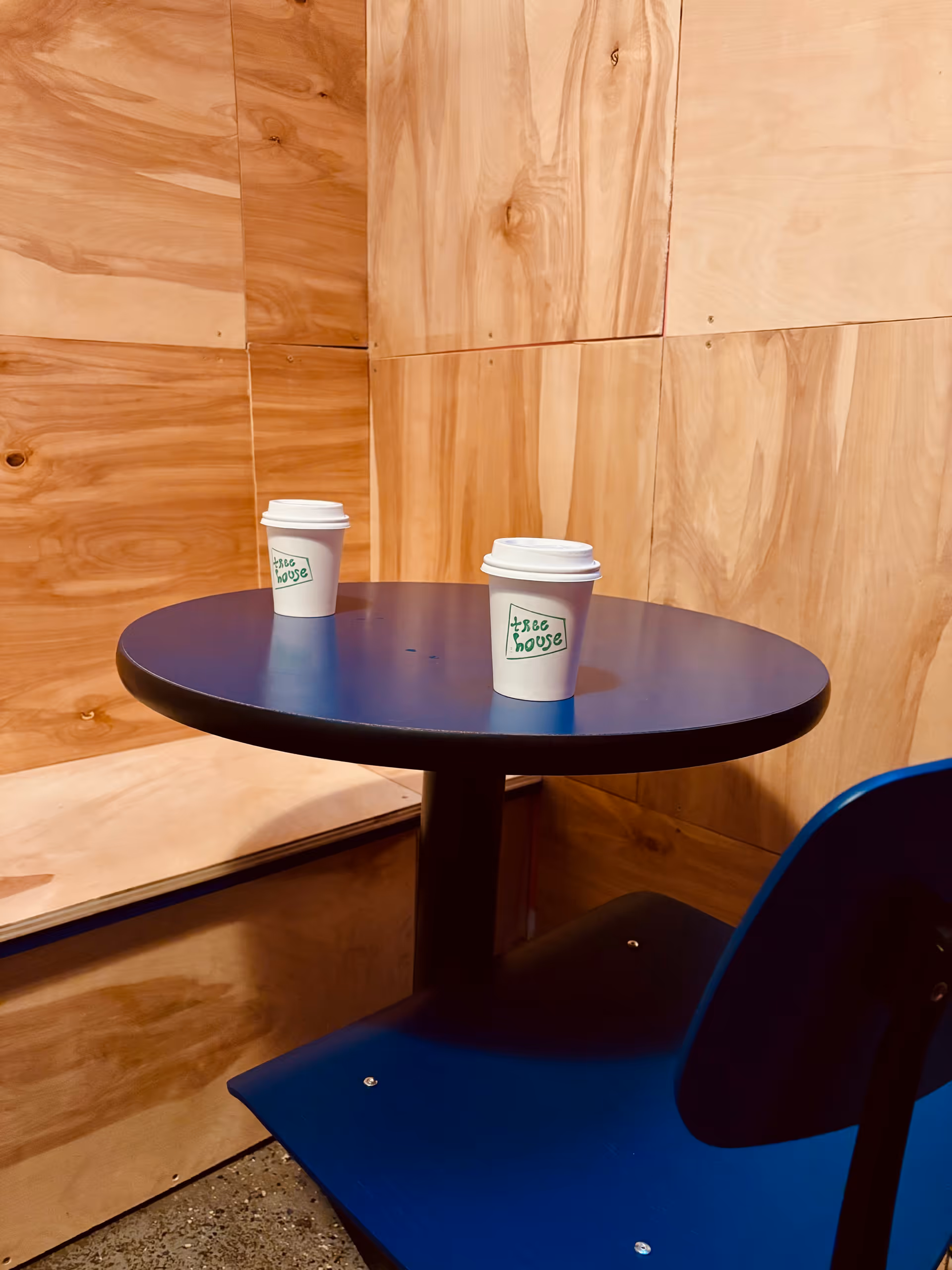 Round blue table with two disposable coffee cups in a wood-paneled interior.