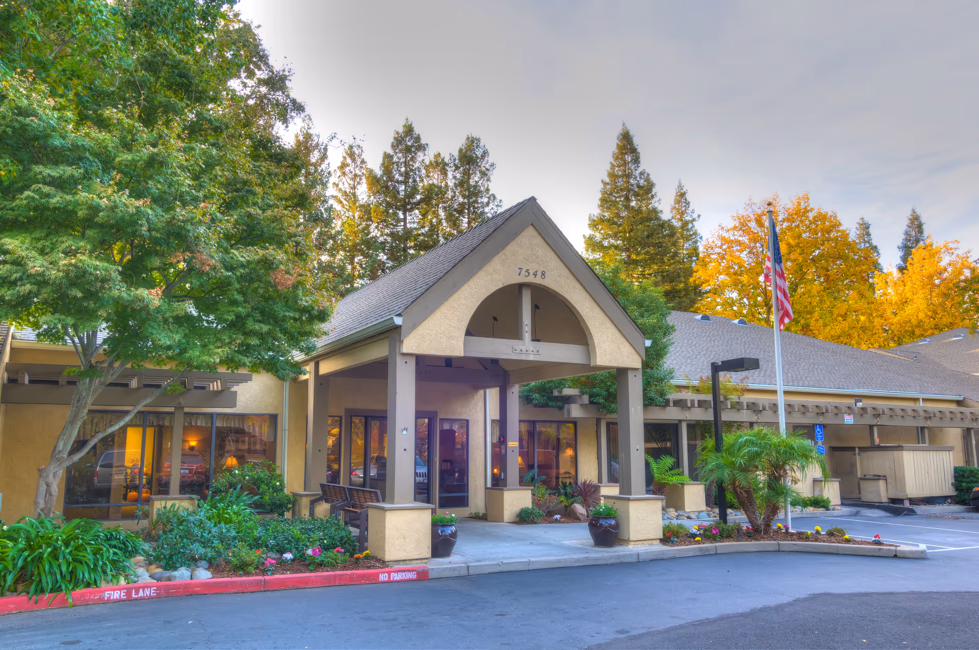 Front view of Elder Care Haven's entrance with trees, plants, and an American flag.