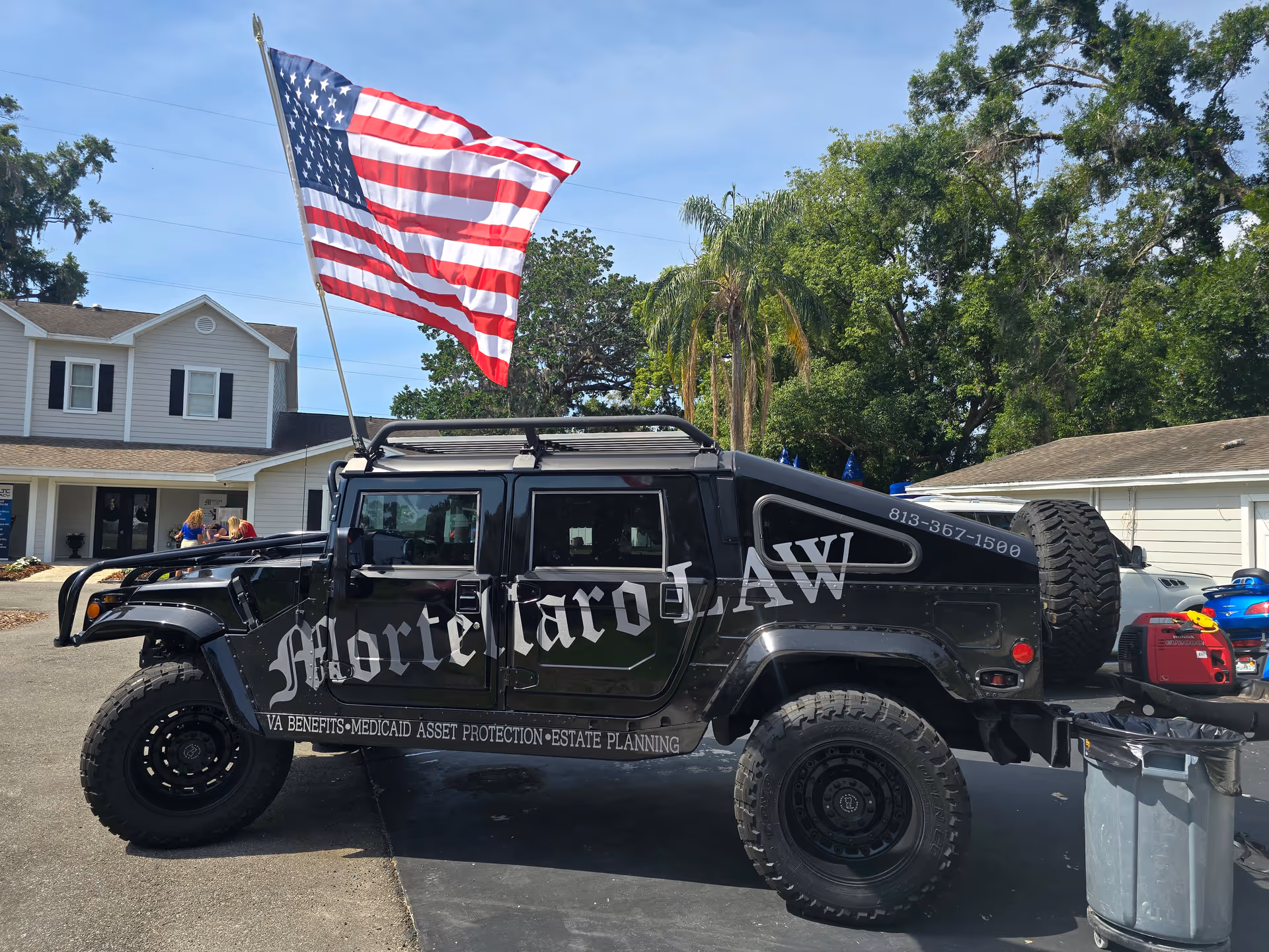 Black off road SUV with large tires and an American flag outside a residential building.
