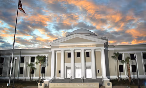 Front view of a grand neoclassical courthouse with tall white columns and a sunlit sky.