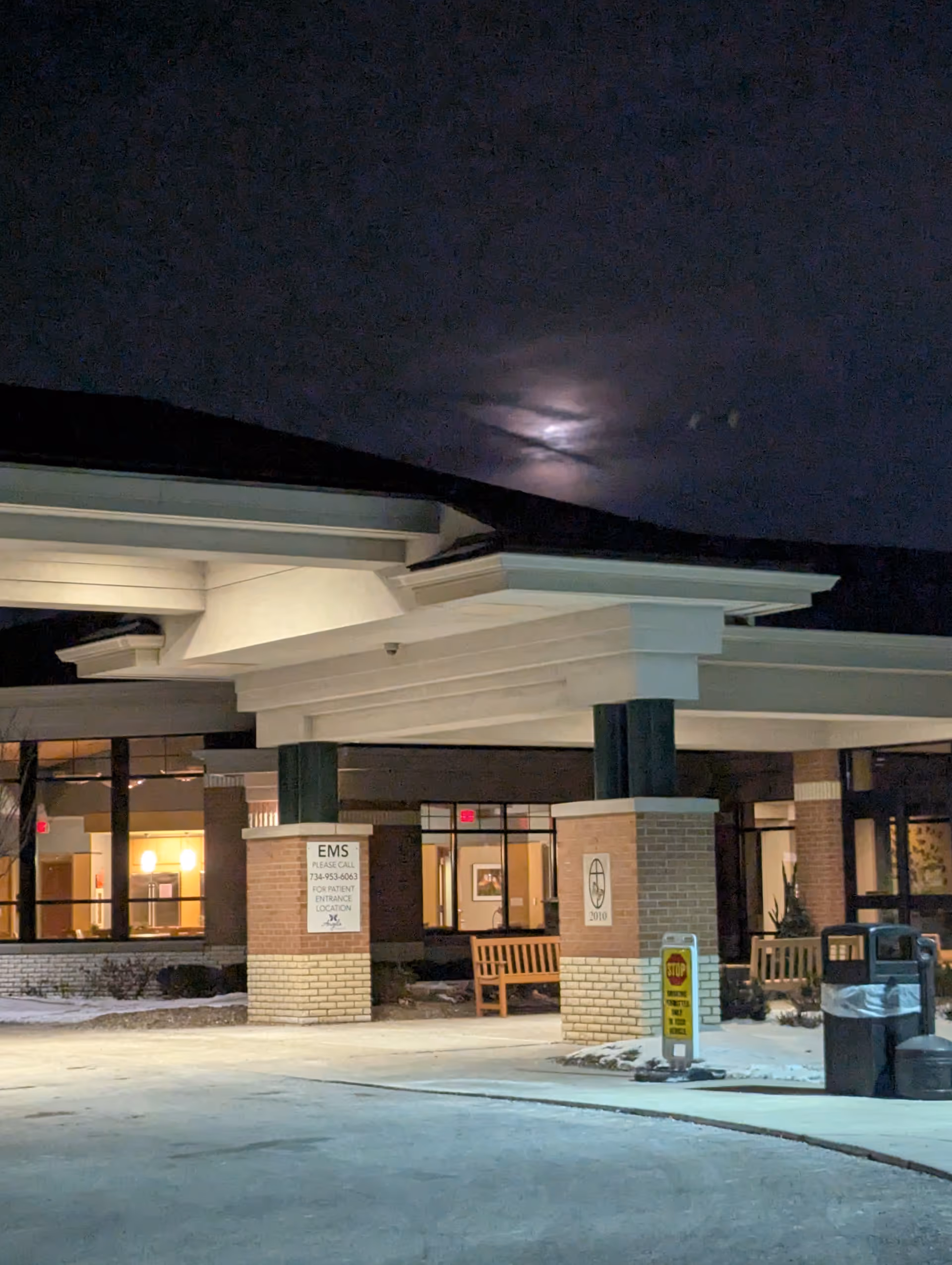 Night exterior view of a senior care facility entrance with benches and signage.