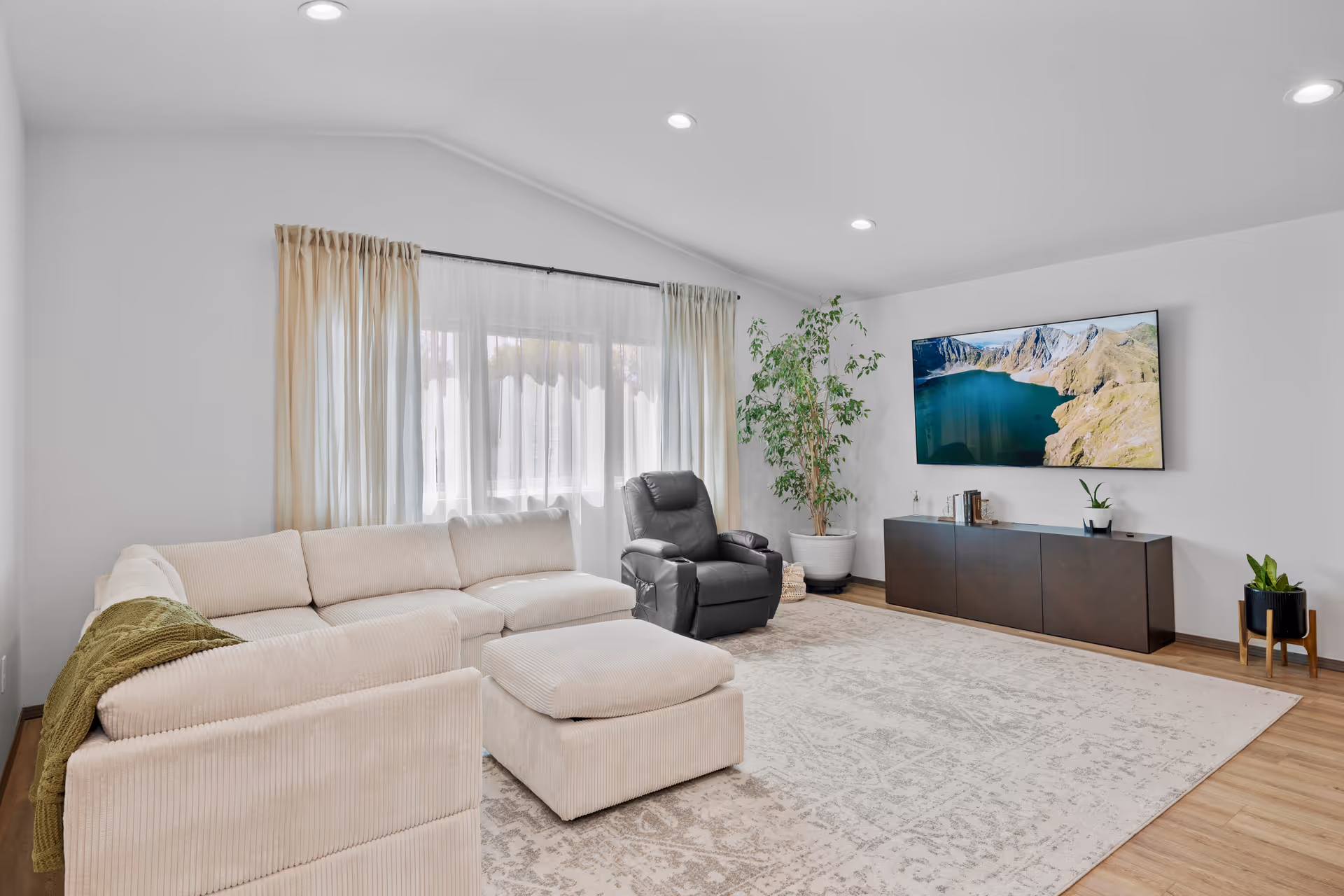 Cozy living room with beige sectional, recliner, TV, rug, and plants.