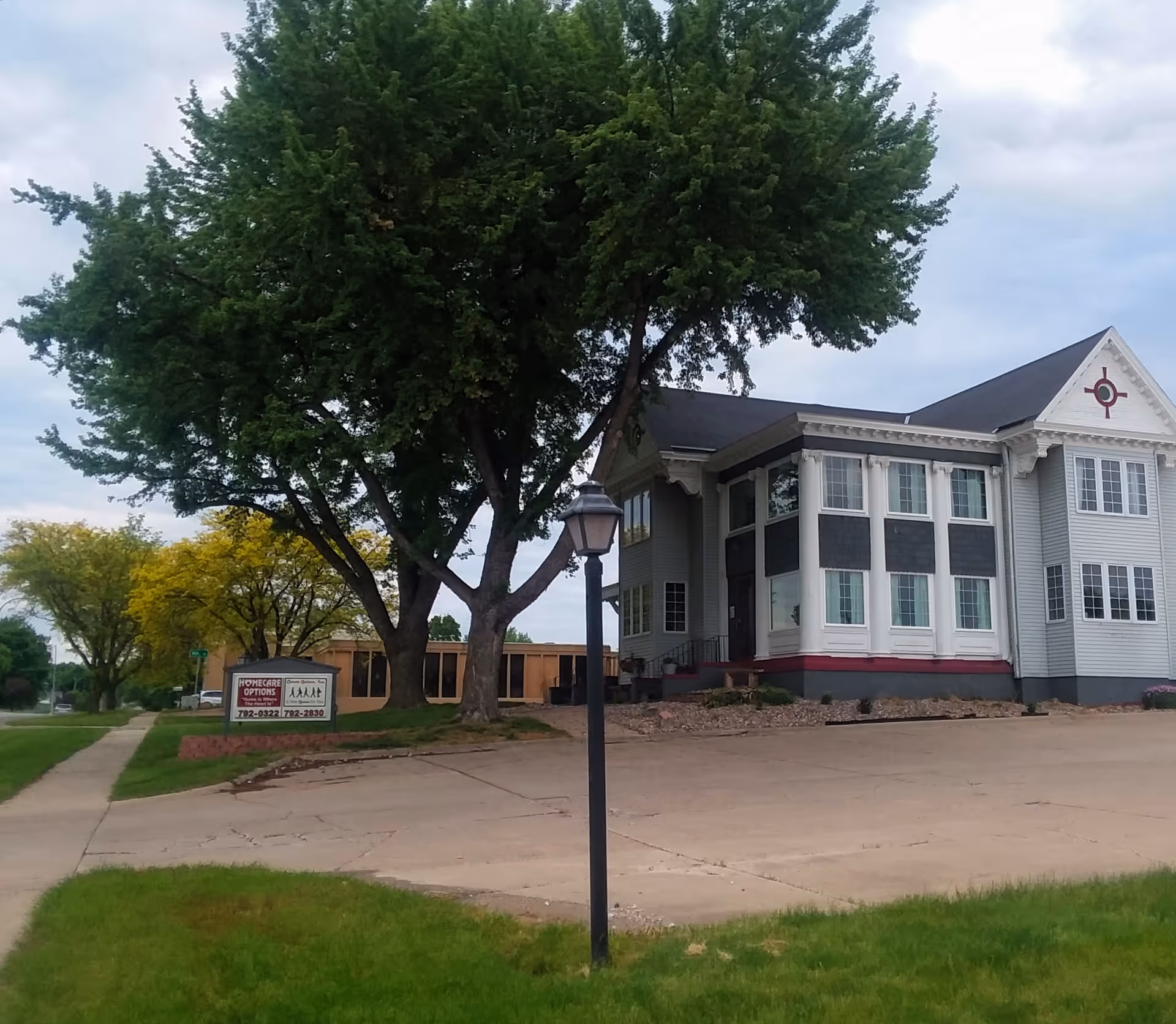Exterior view of a senior facility with a large tree, lamppost, and sign.