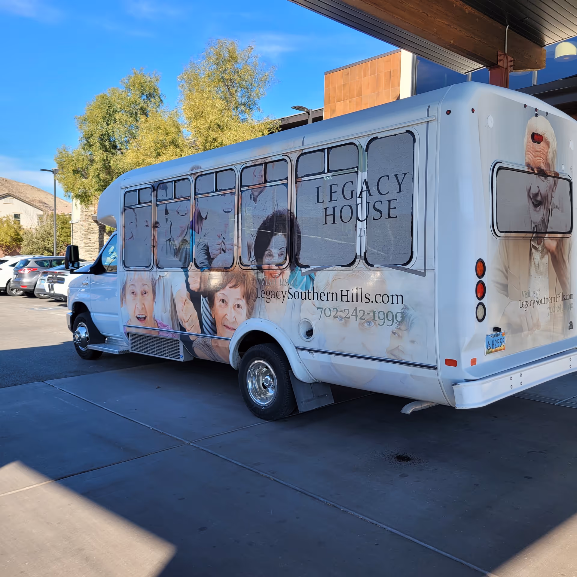 A white Legacy House shuttle bus with elderly-faced graphics parked outside a building.