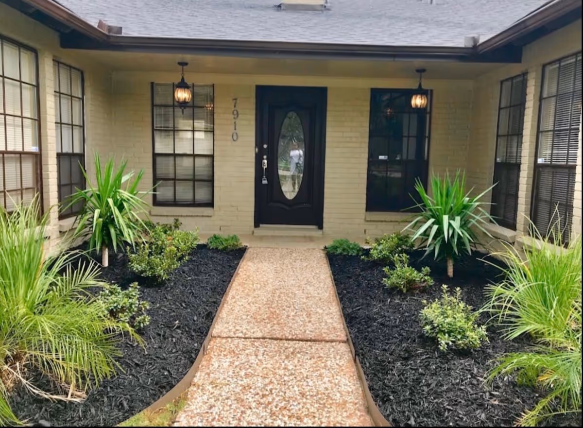 Front entrance of a beige brick senior living facility with a walkway and landscaping.