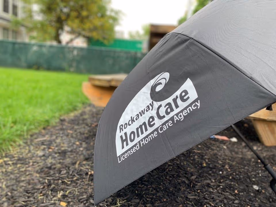 Close-up of a Rockaway Home Care umbrella outdoors on mulched ground near grass.