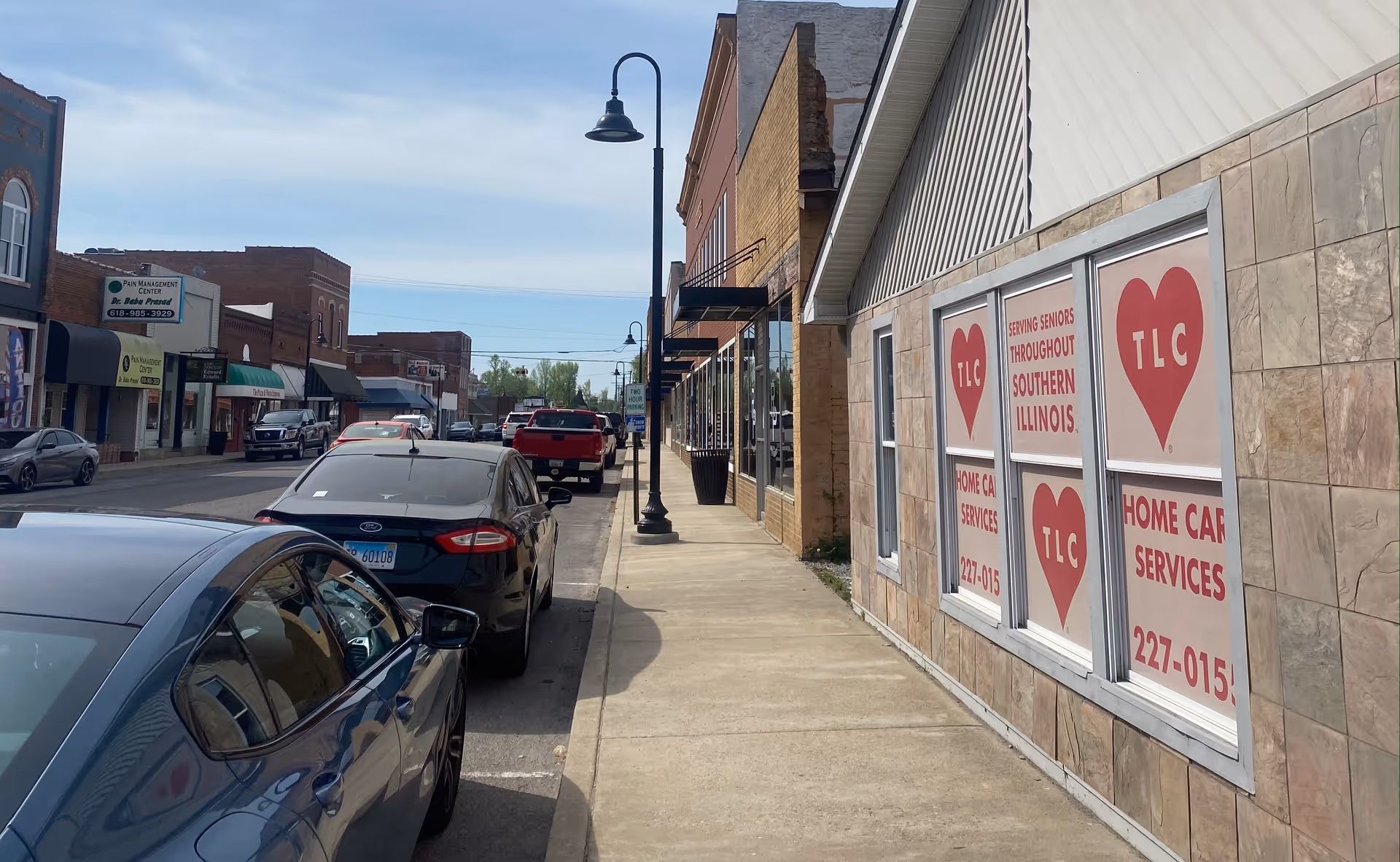 Street view of TLC Home Care Services storefront along a sidewalk with parked cars.