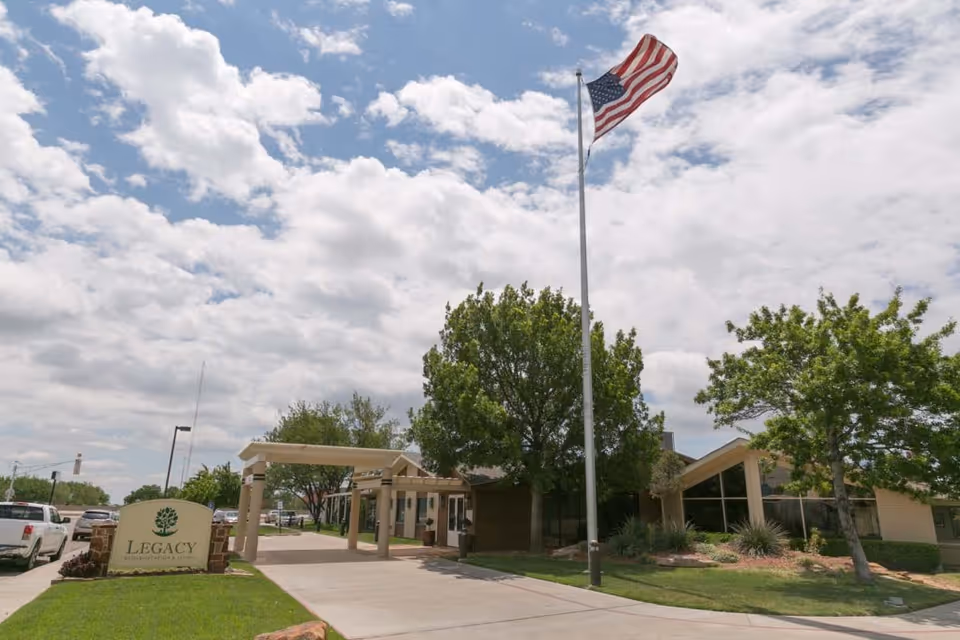 Legacy Rehabilitation and Living exterior with entrance canopy, flagpole, and trees.