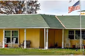 Front view of a yellow single-story senior care building with porch seating.