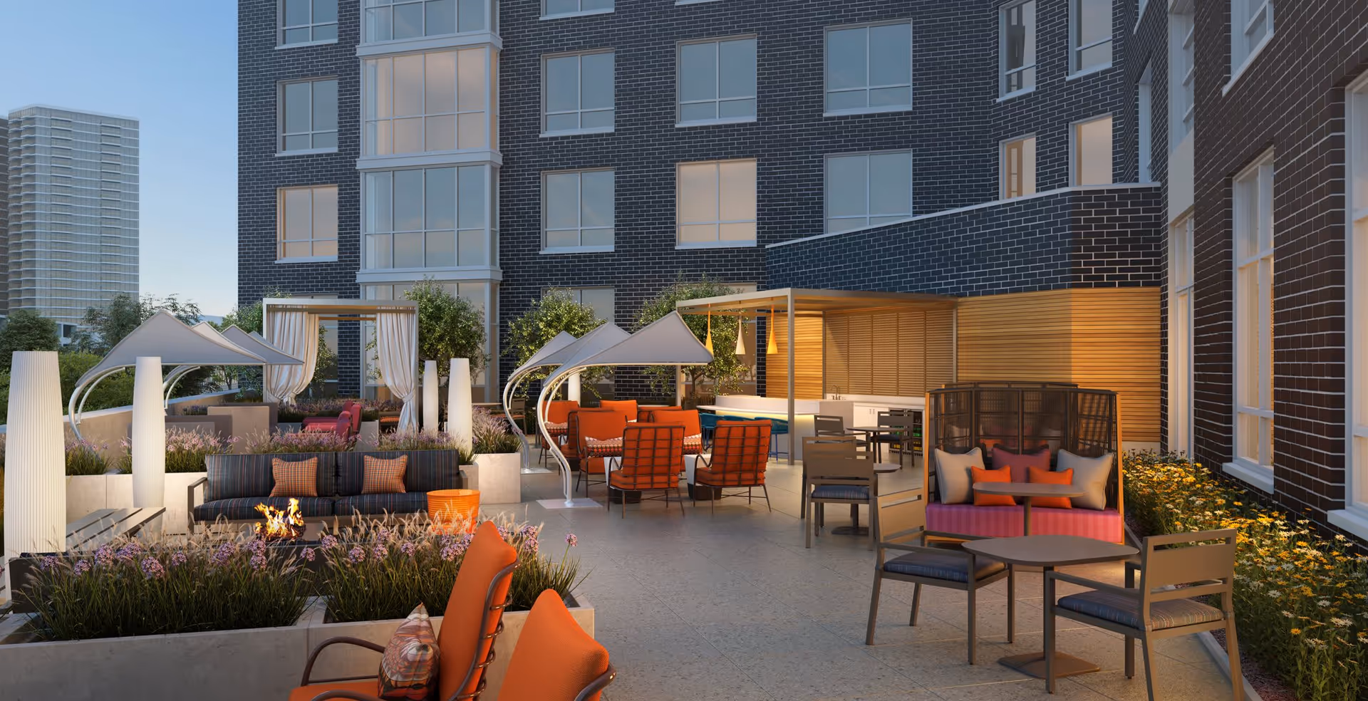Outdoor courtyard with lounge seating, cabanas, a fire pit and dining tables alongside a multi-story brick building.