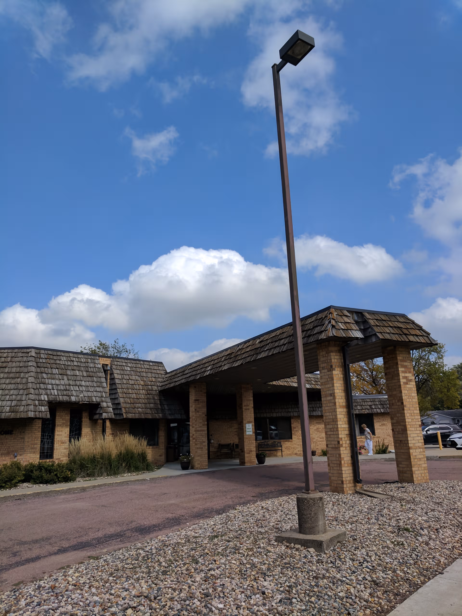 Exterior view of Bethesda of Beresford with brick entrance, canopy, and tall streetlight under blue sky.