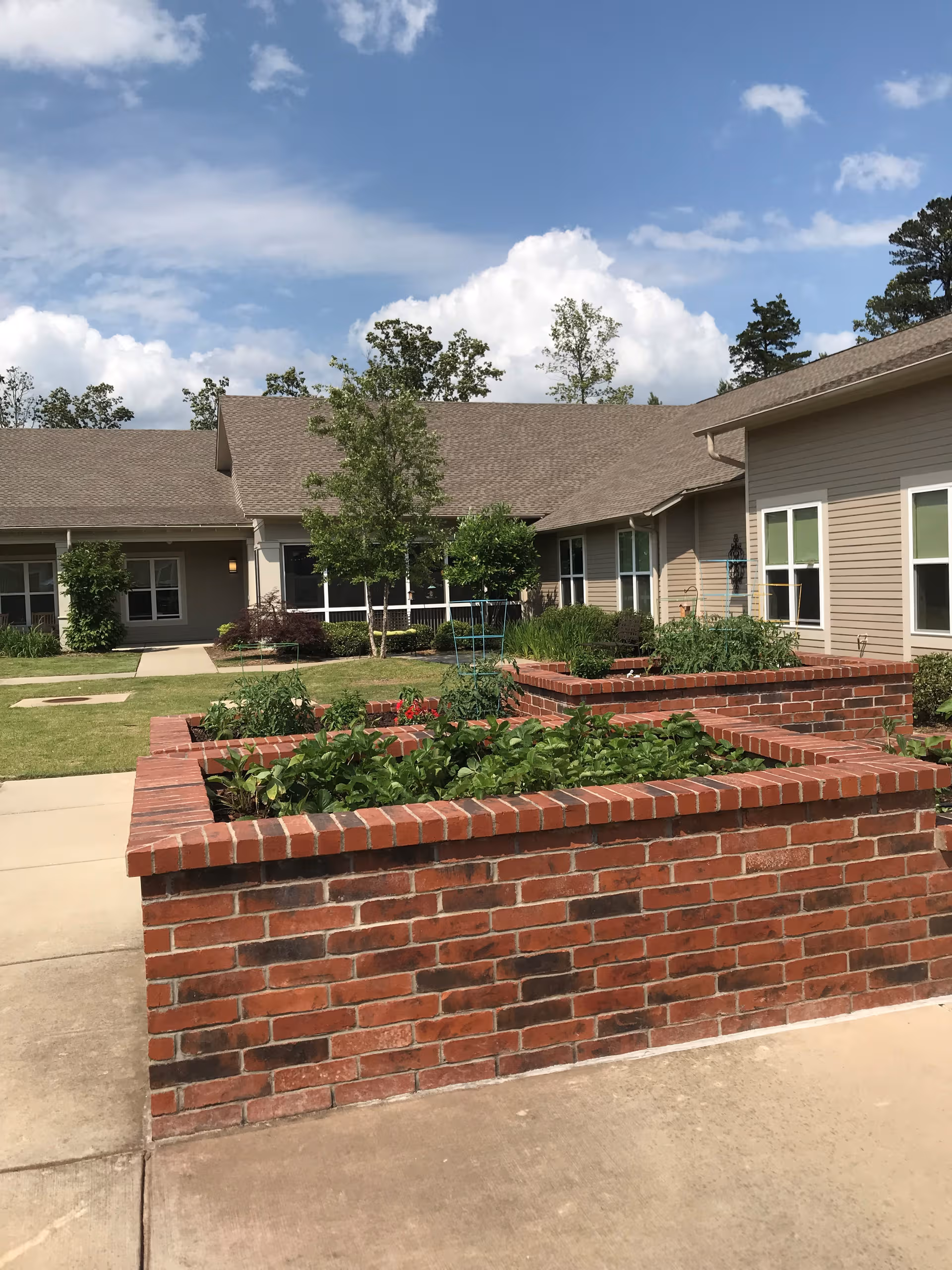 Exterior view of a memory care facility with brick planters and manicured landscaping.
