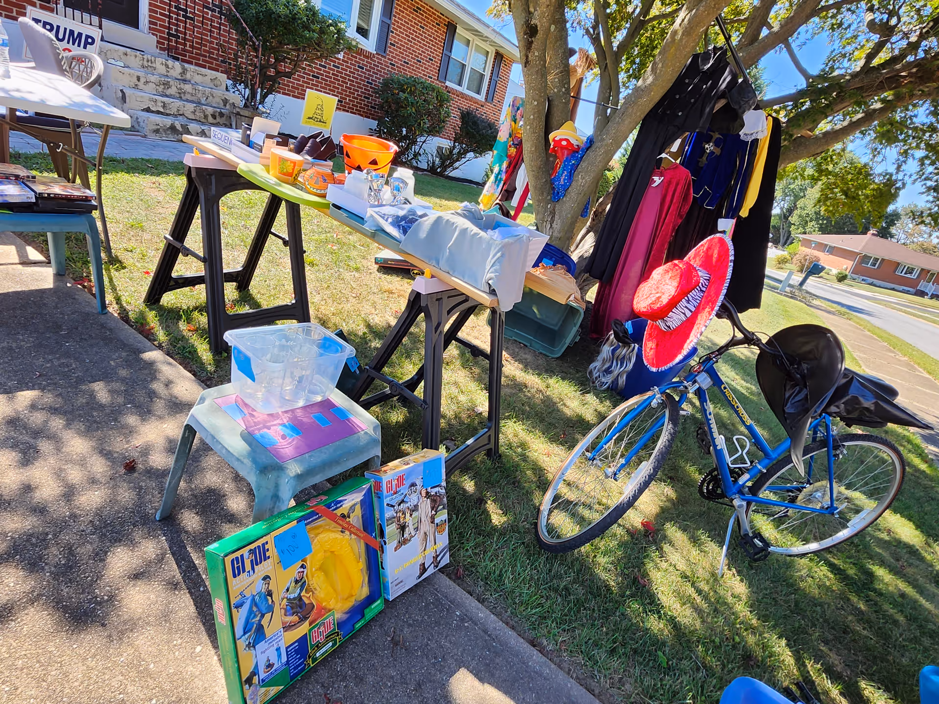 Outdoor yard sale setup outside a CarePlus Health facility with tables, clothing, and a bike.