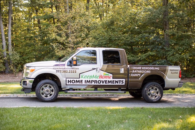 Exterior KeepMeHome Home Improvements truck parked by a tree-lined roadside.