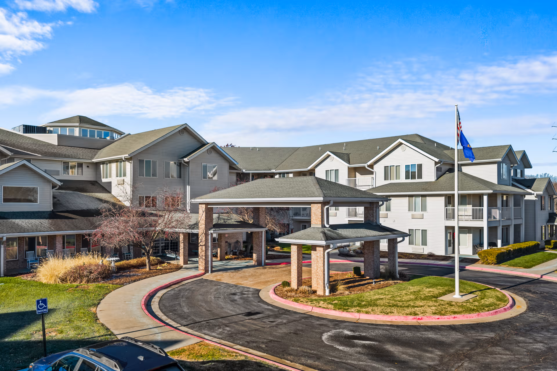 Wide view of Holiday Grasslands Estates exterior with circular driveway, entrance canopy, and flagpole.