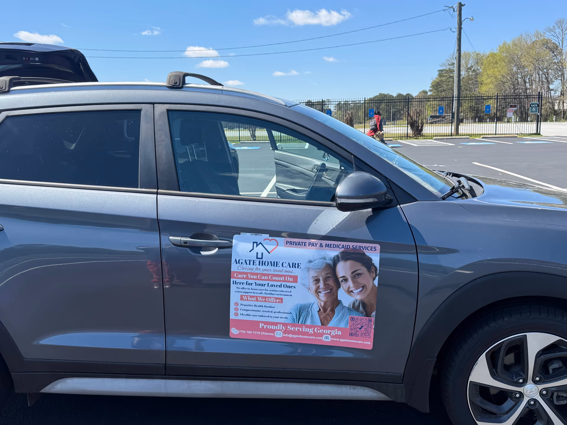 Gray SUV in a parking lot with Agate Home Care promotional sign featuring smiling seniors.