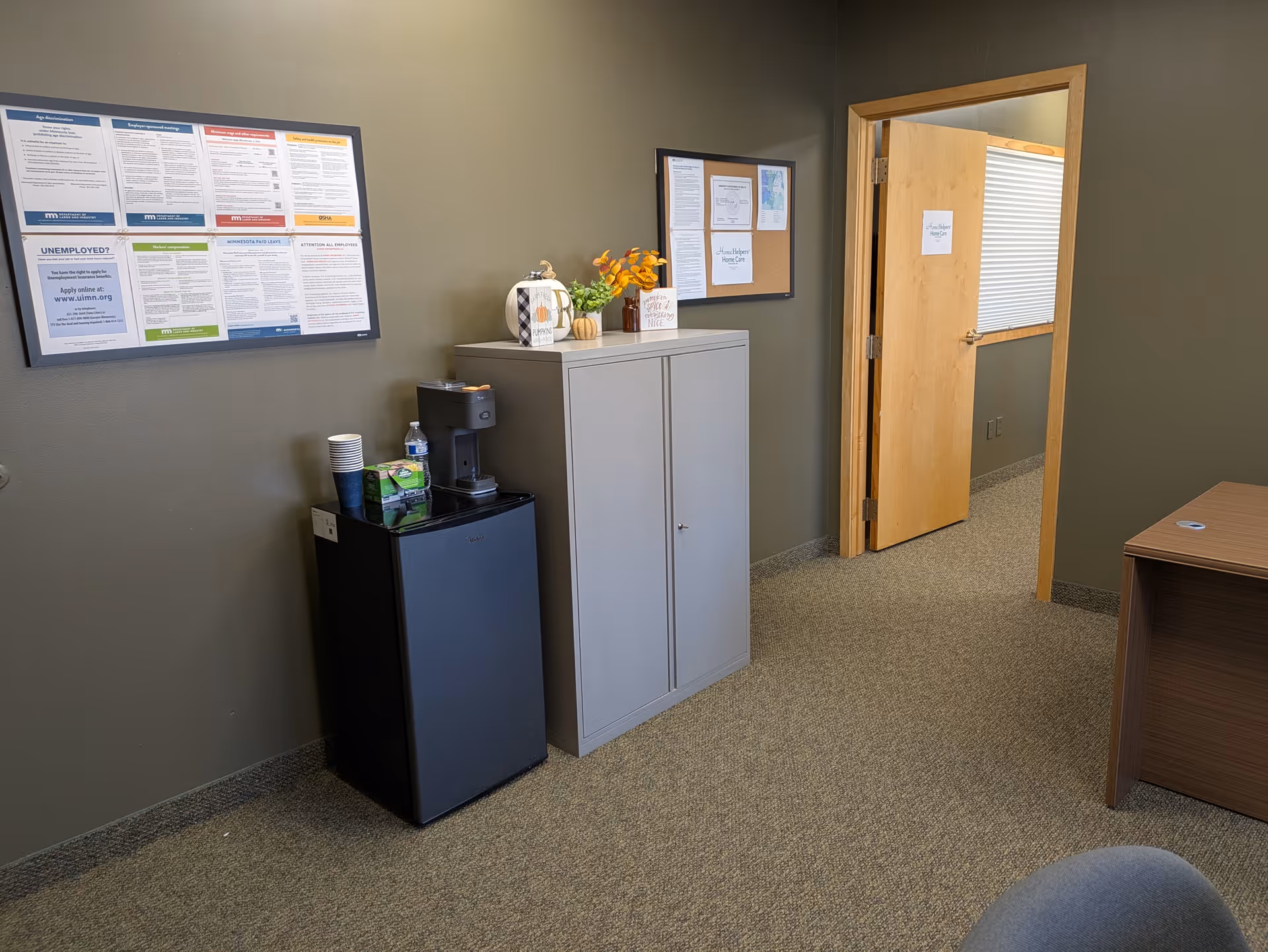 Interior office area with a coffee station, cabinet, bulletin boards, and doorway.