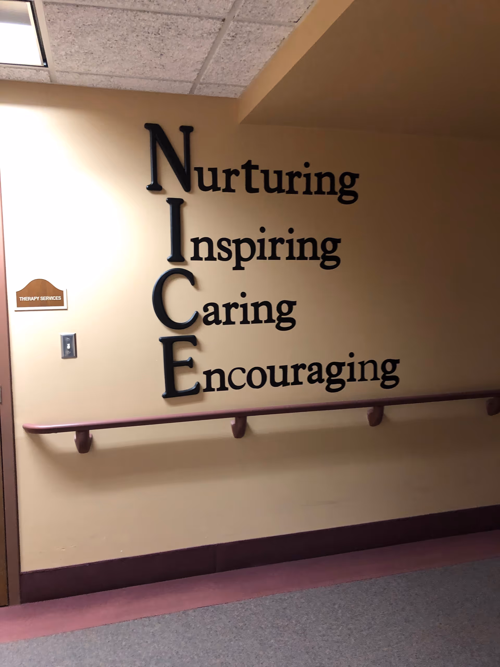 Interior hallway wall displays vertical NICE acronym with Nurturing, Inspiring, Caring, Encouraging.