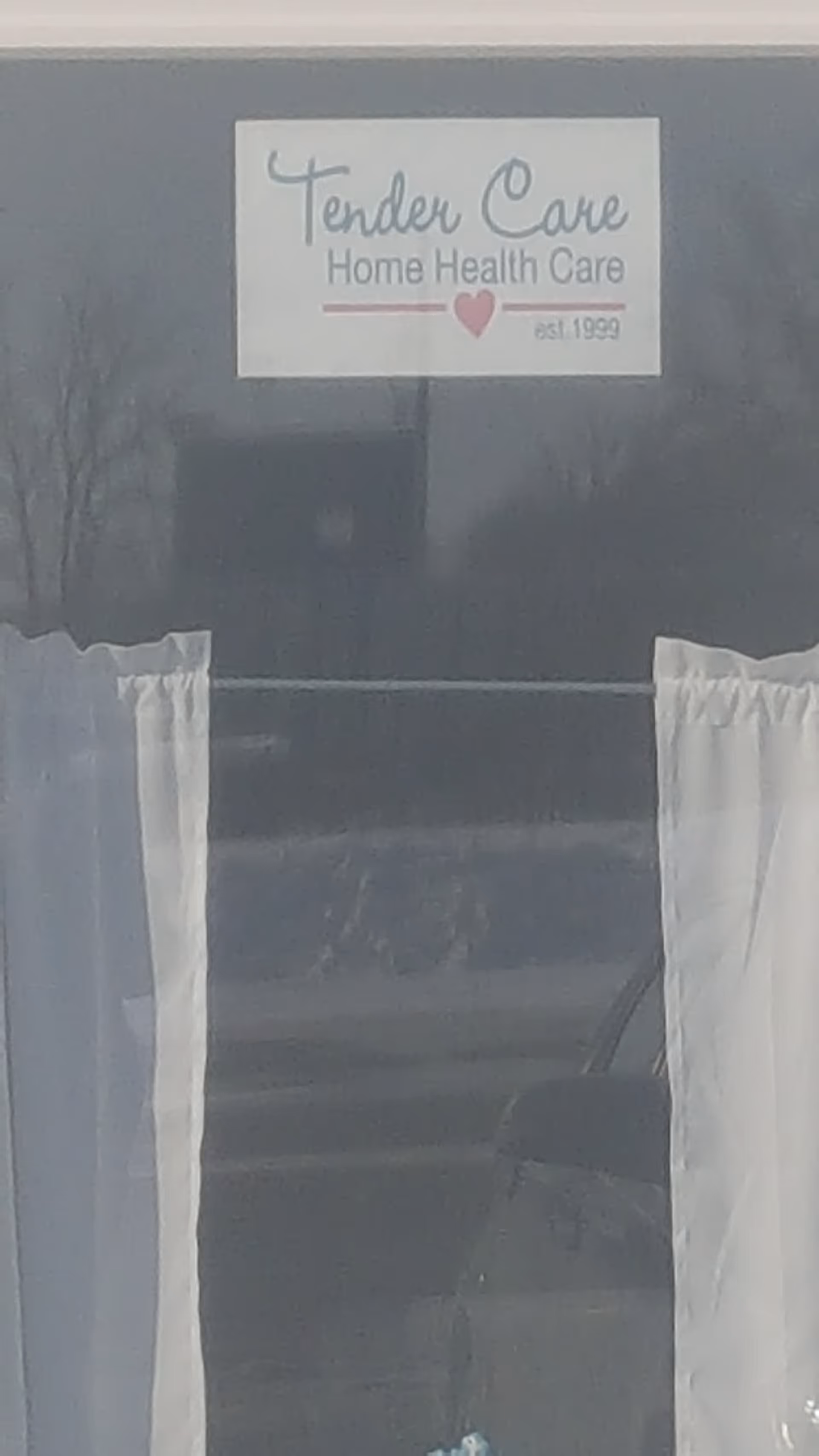 Sign reading Tender Care Home Health Care on a window with white curtains.