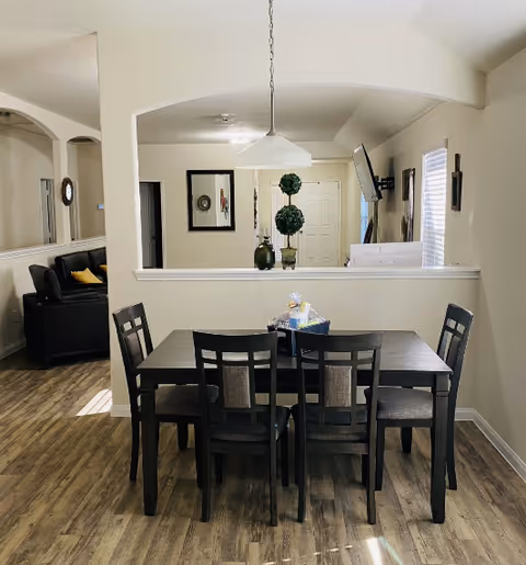 Dining table with six chairs in a bright dining area, open to living room.