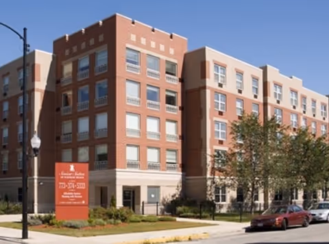 Exterior view of a brick senior living building with a red sign on a street corner.