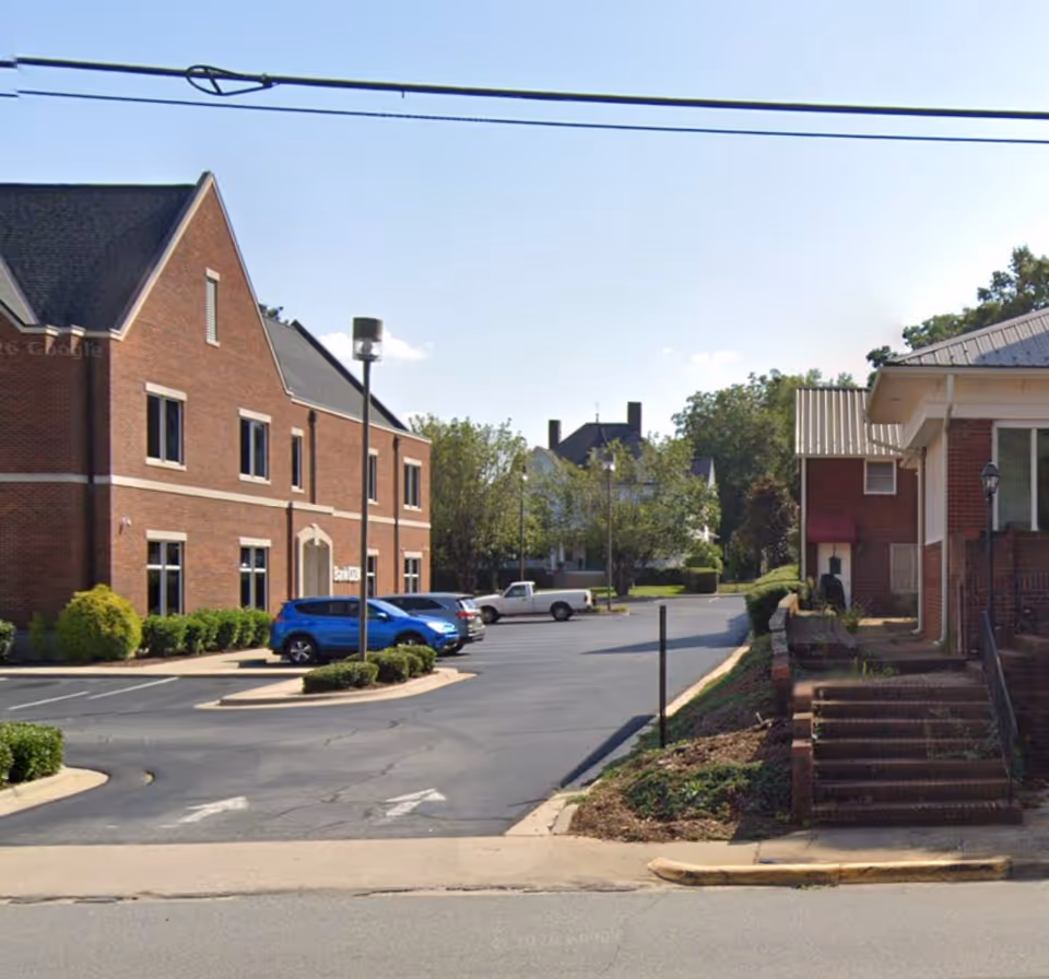 Exterior view of a brick senior care facility with parking lot and entrance stairs.