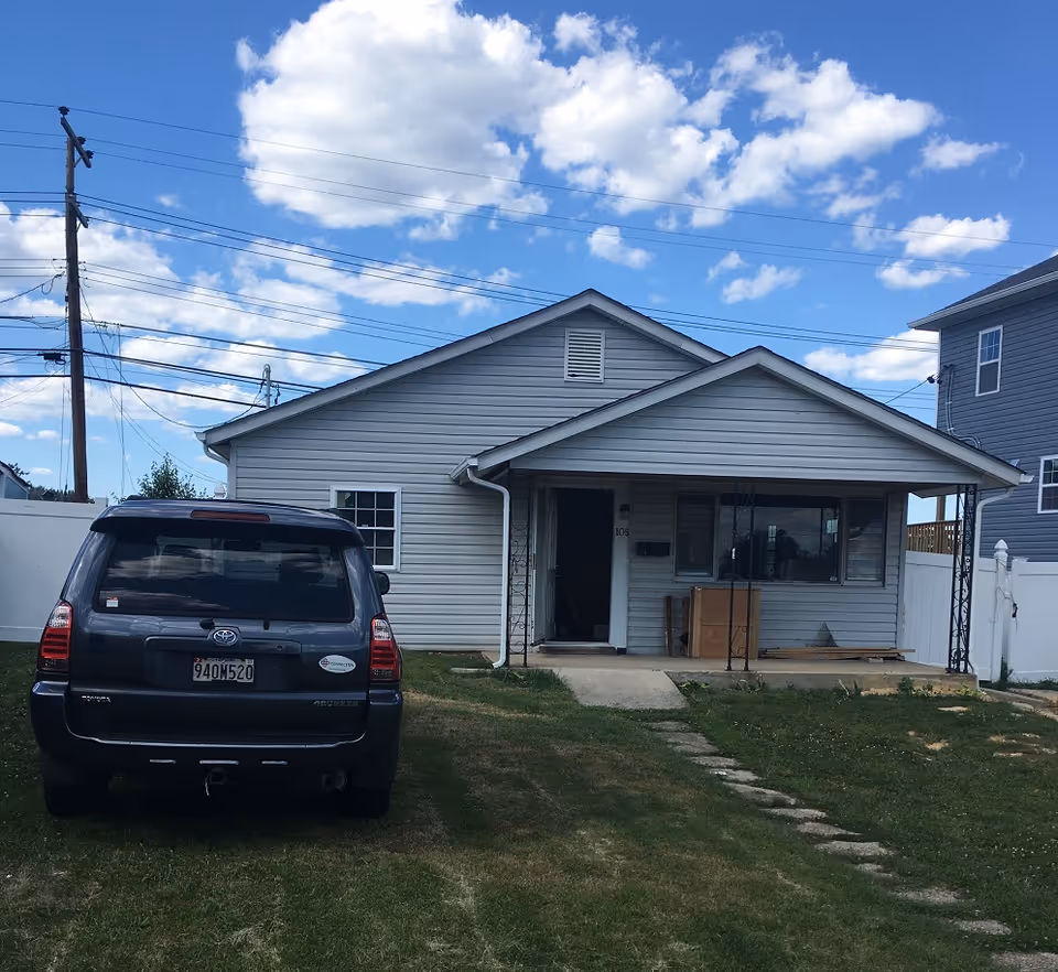 Front view of a single-story building with a parked SUV and a small porch.