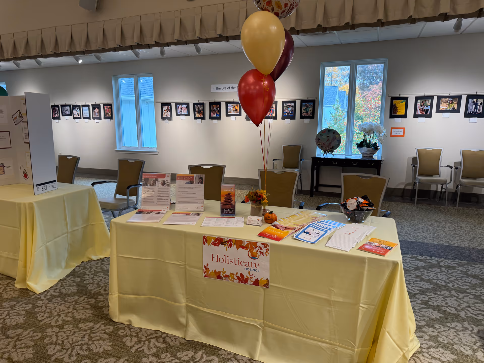 Interior event area with a long yellow-draped table, balloons, and wall-mounted photos.