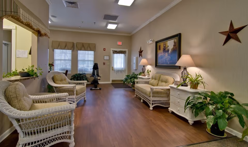 A welcoming senior living facility lounge with wicker chairs, couches, lamps, and plants.