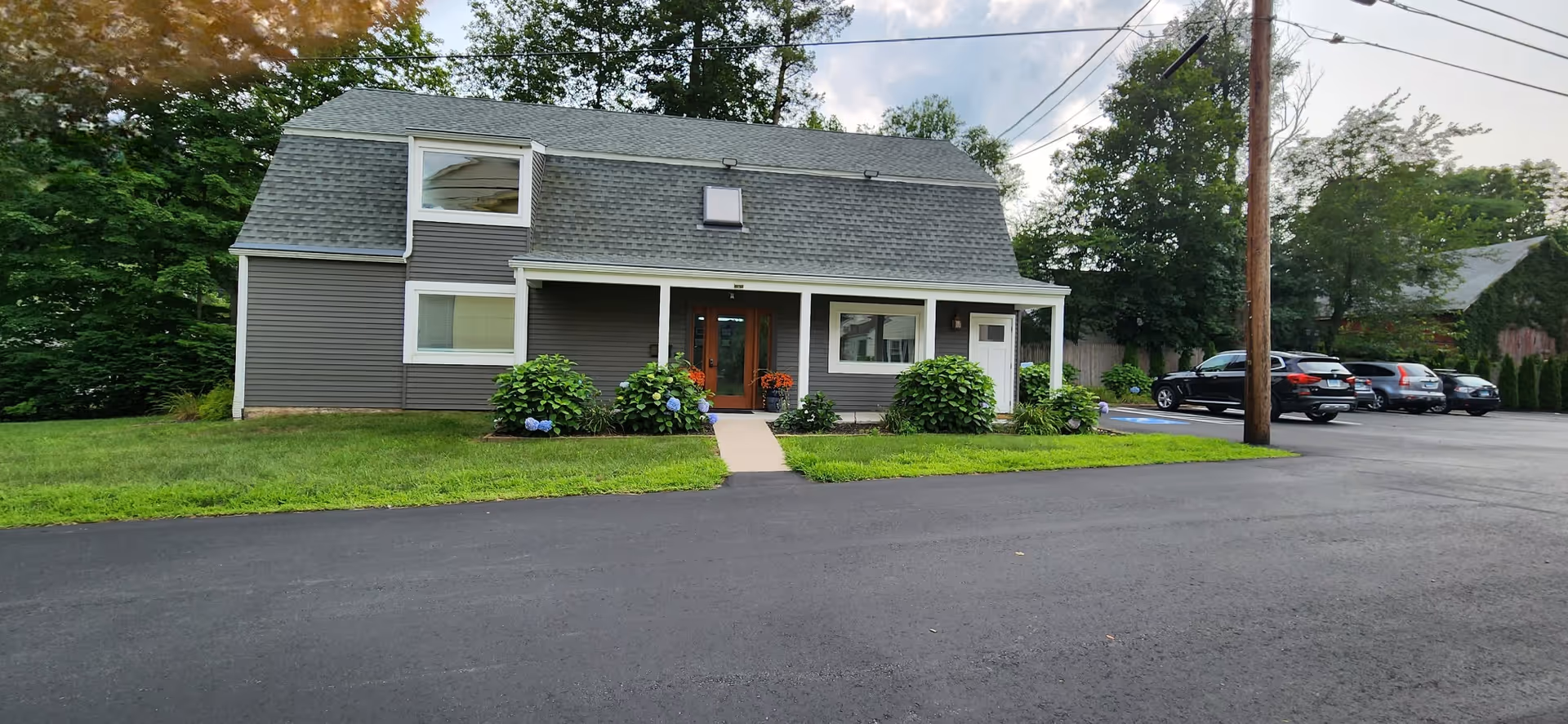 An exterior view of a gray, two-story senior care facility with a front entrance and parking.