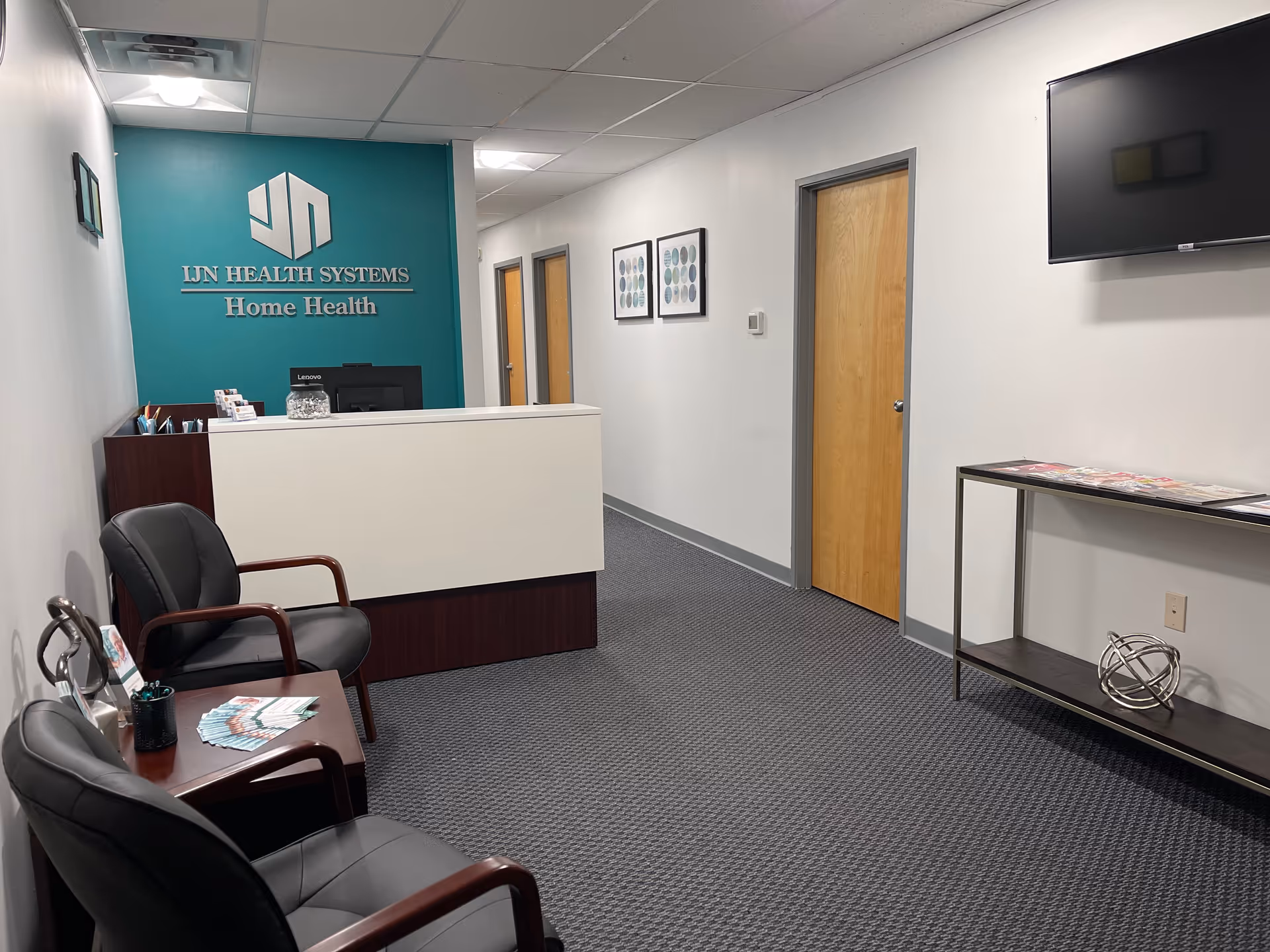Reception area with teal wall sign, desk, chairs, and hallway in a medical facility.