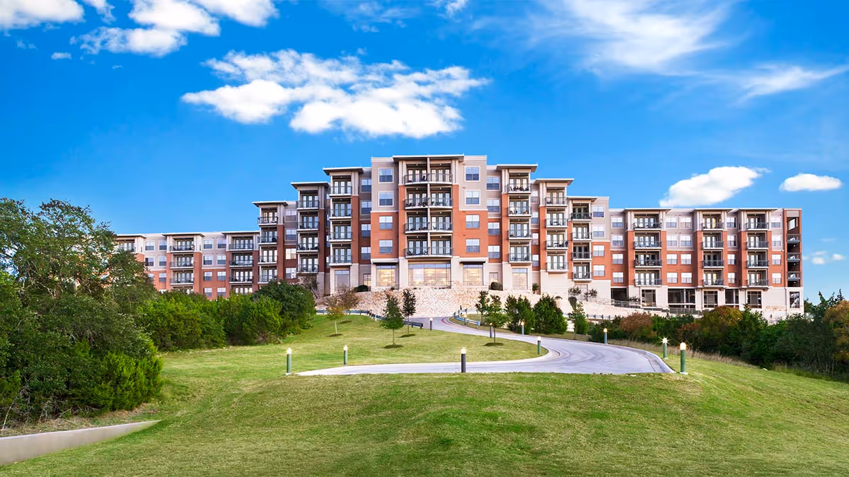 Large multi-story brick senior living building on a grassy hill with a curved driveway.