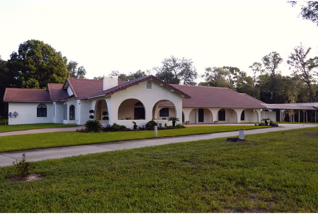 Single-story white building with a red-tiled roof and arched entryways on a grassy lawn.