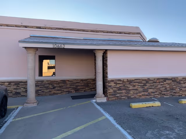 Exterior view of a pastel pink building with stone accents and a small service window.