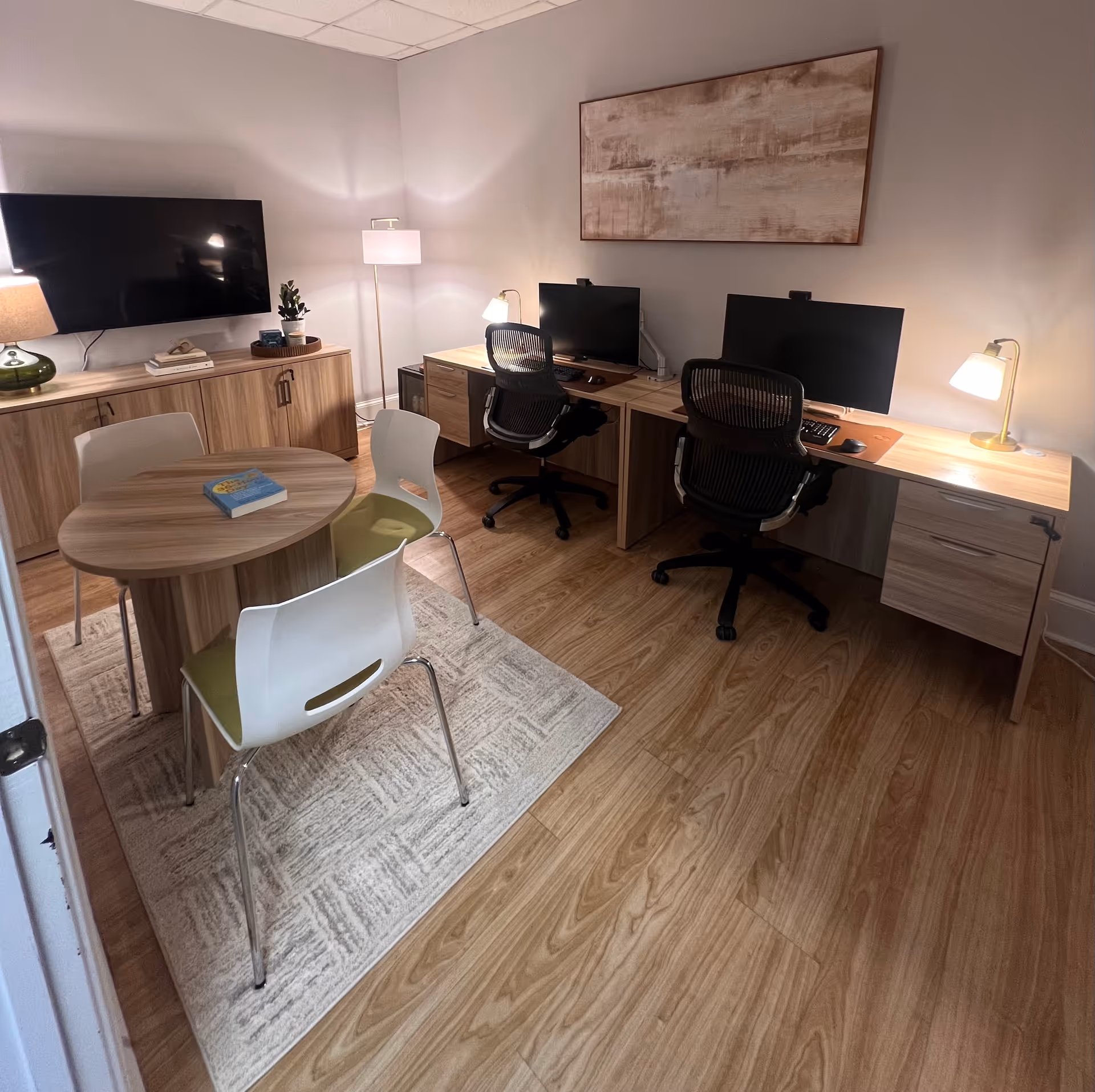 Interior office area with two desks, computers, a TV, and a round meeting table.