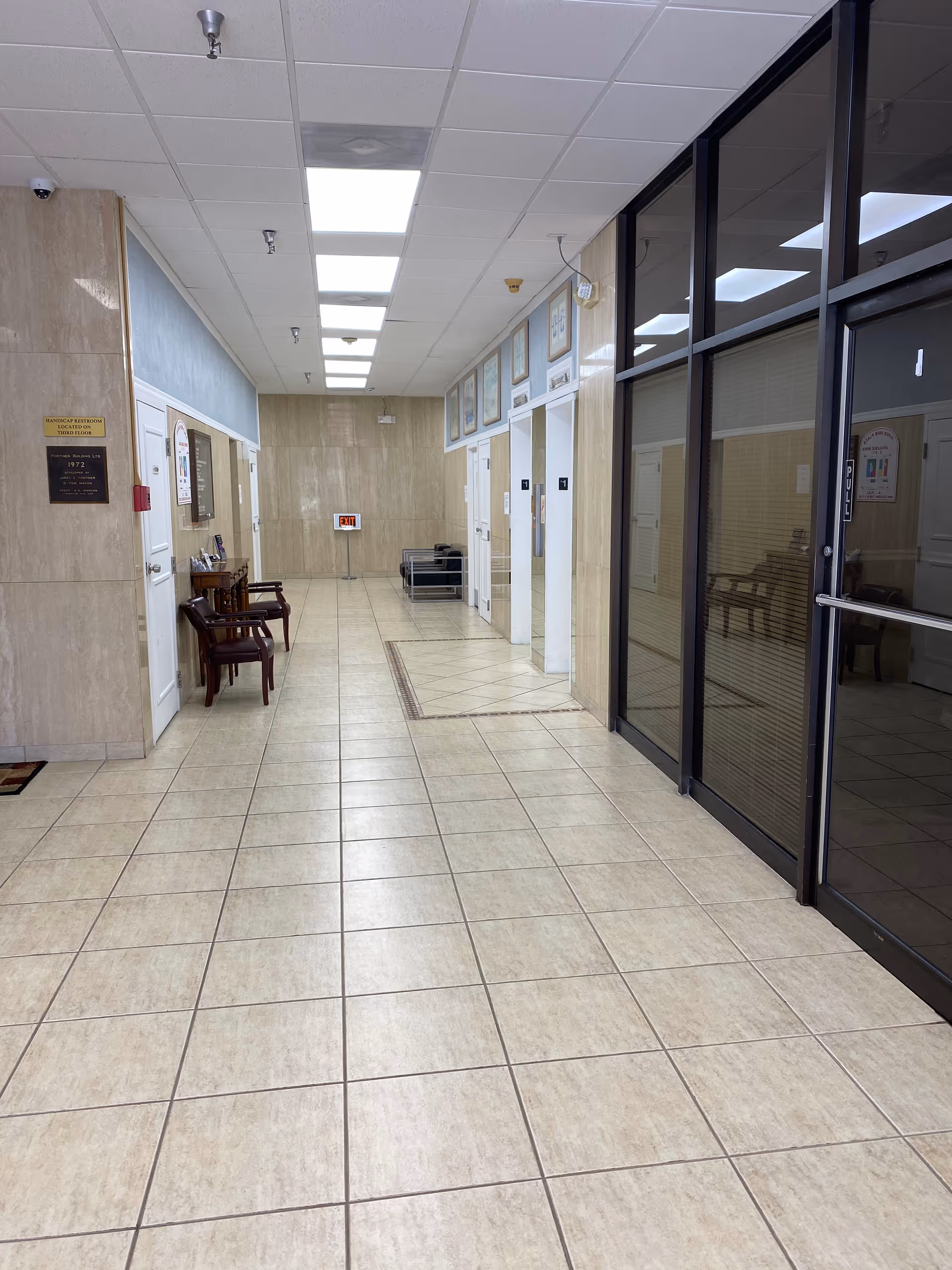 Long tiled corridor of a senior facility with glass doors and chairs.