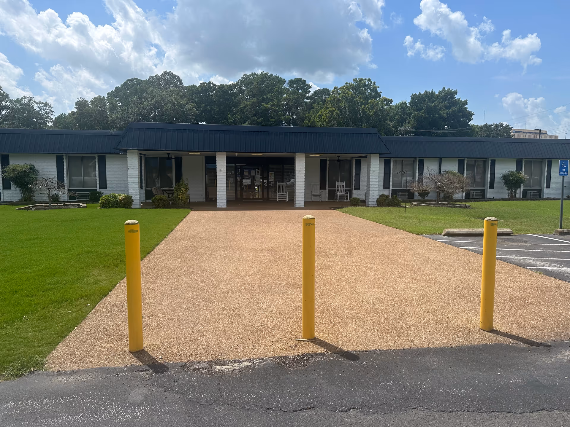 Senior living facility entrance with a covered walkway, yellow bollards, and front lawn.