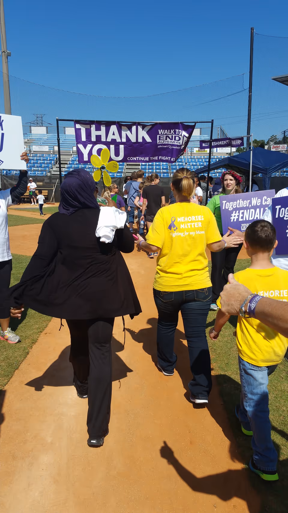 People walk along an outdoor track at a charity event with banners.