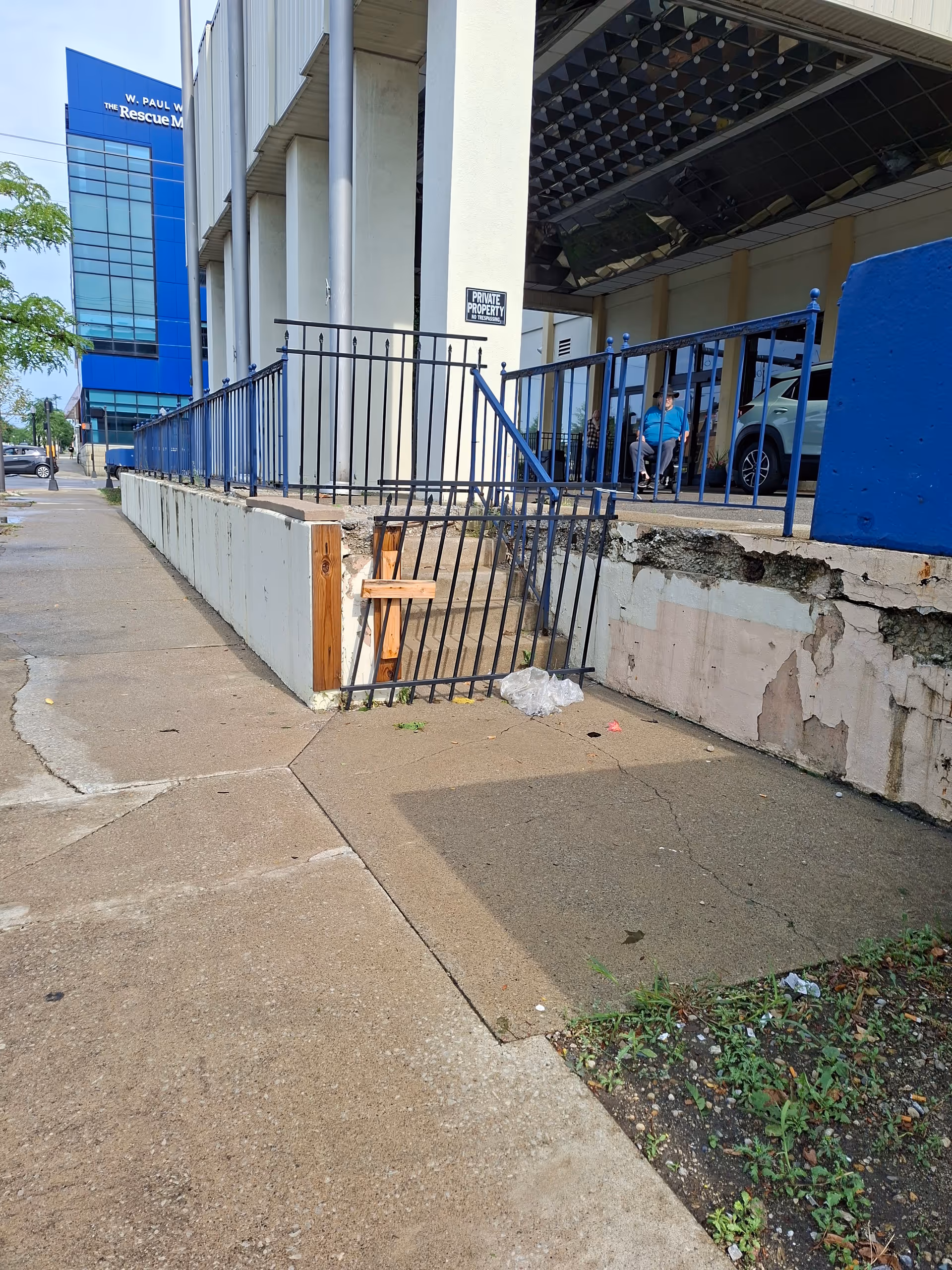 Outdoor view of a senior living facility entrance with stairs, ramp, and blue railing.