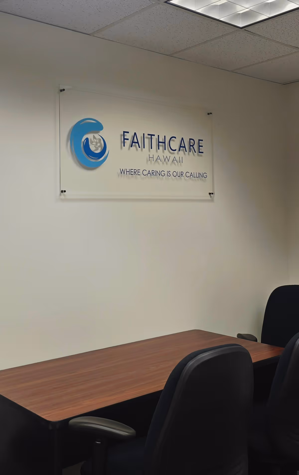 Office conference area with FaithCare Hawaii sign on the wall and a wooden desk.