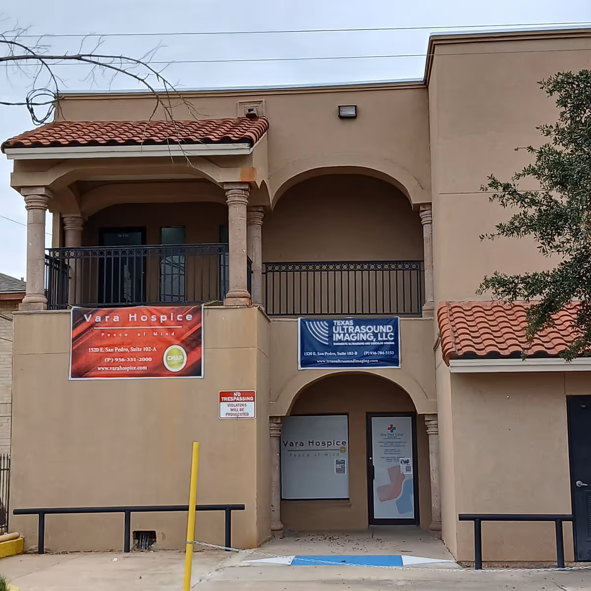 Two-story tan building with arches, balconies, and banners for Vara Hospice and ultrasound imaging.