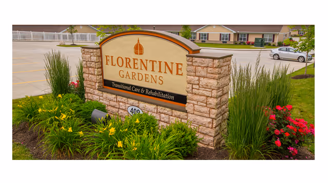 Florentine Gardens exterior sign with stone surround and landscaped plants by the parking lot.