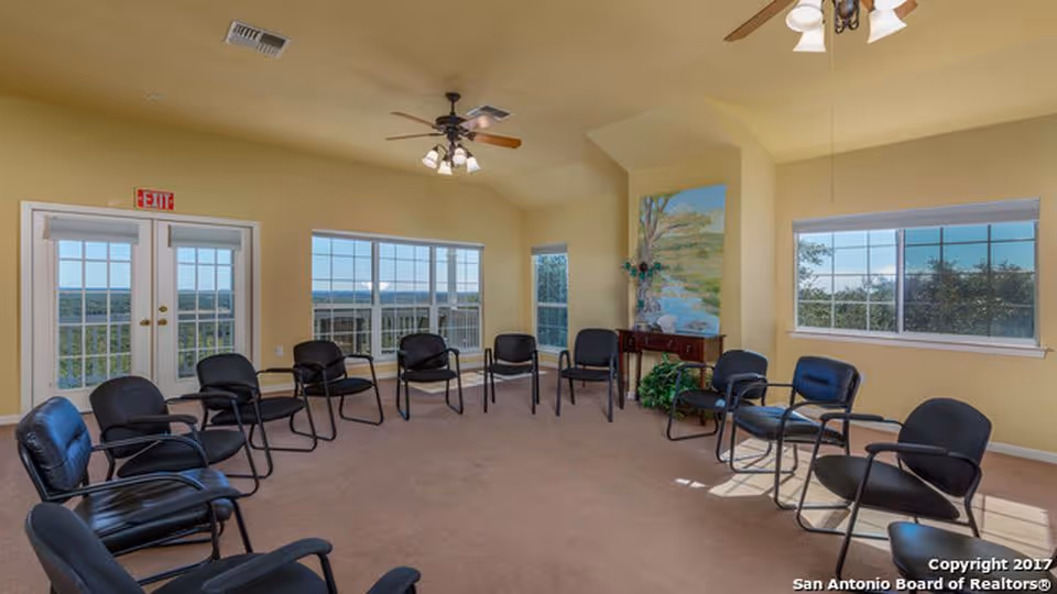 Sunlit senior living common room with arranged black chairs in a circle.