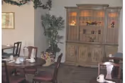 Dining room with round tables, chairs, a wooden cabinet, and potted plants.
