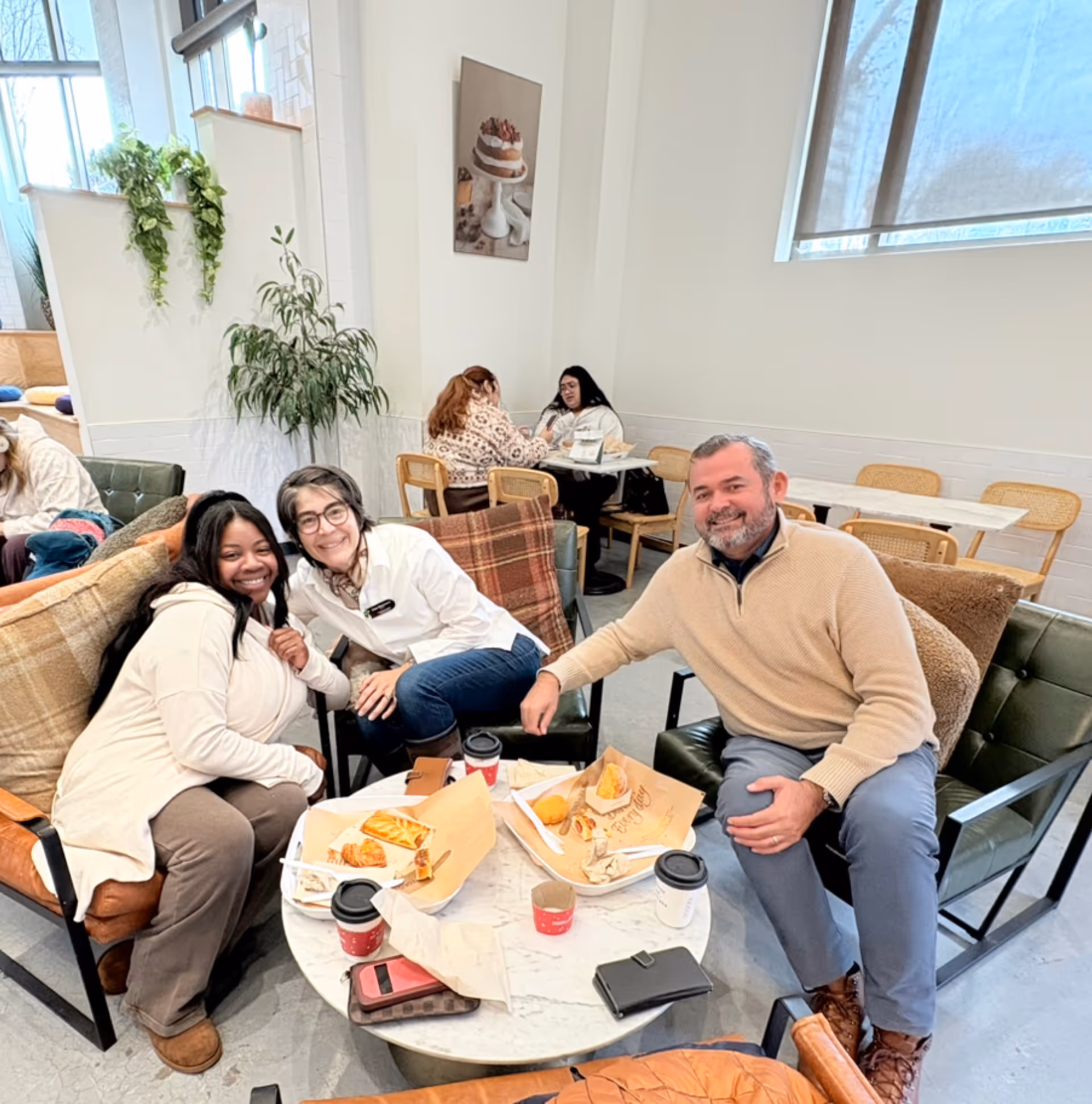 Three adults lounge around a round table with snacks in a bright senior living lounge.