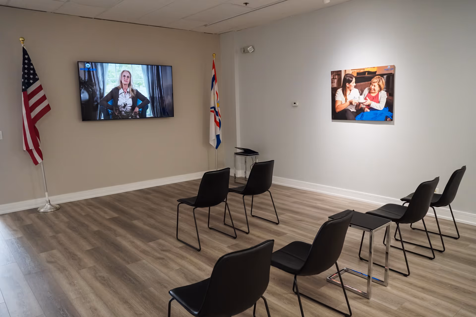 A waiting room with chairs, two flags, a wall-mounted TV, and a photo on the wall.