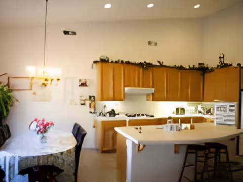 Open kitchen and dining area with wooden cabinets, a central island with stools, and a table topped with a floral centerpiece.
