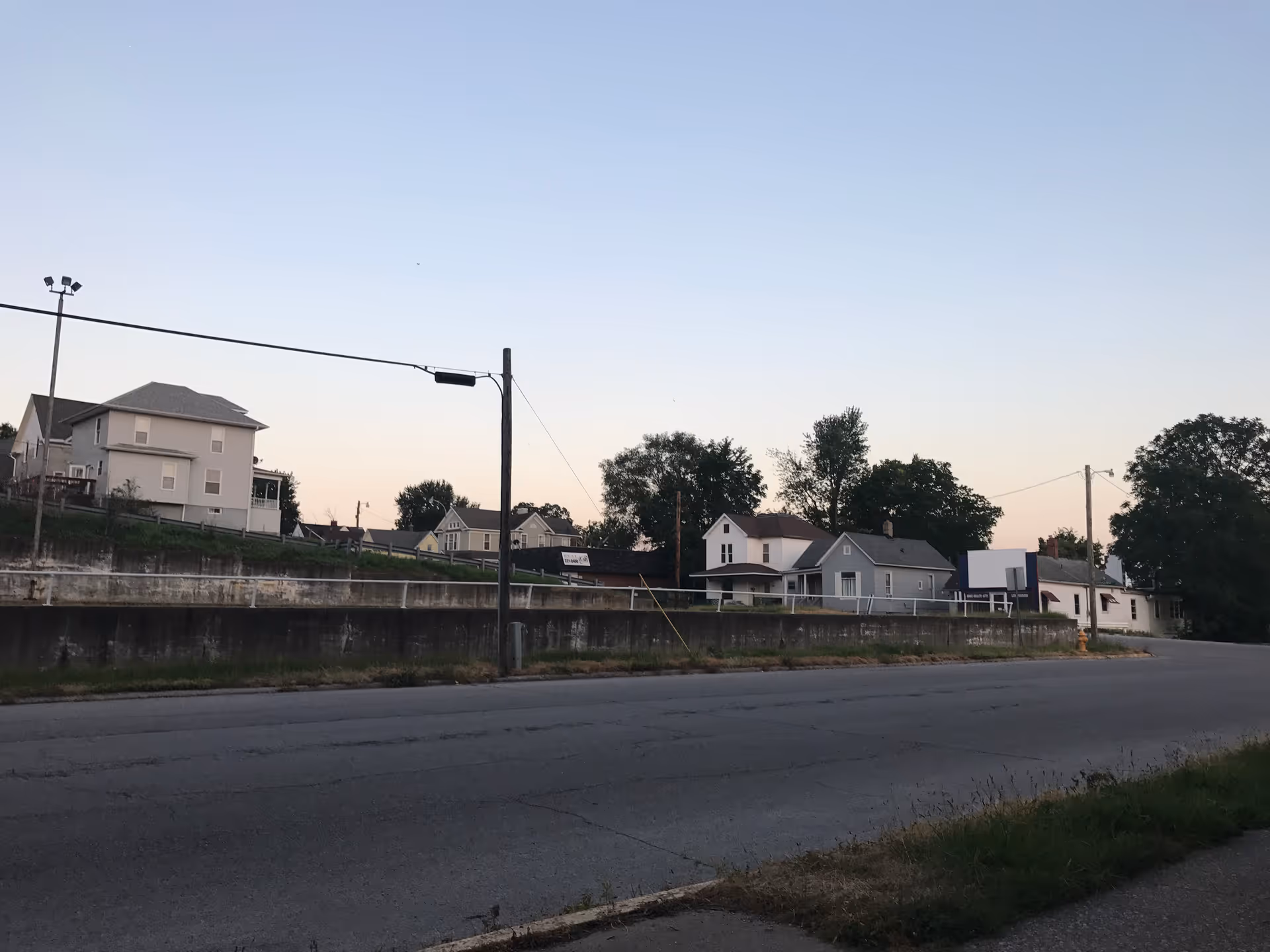 Wide street view of residential buildings with a low retaining wall and utility poles.