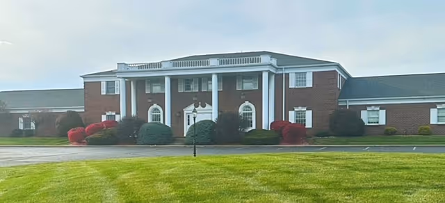 Brick senior living facility with white columns and manicured shrubs at the entrance.